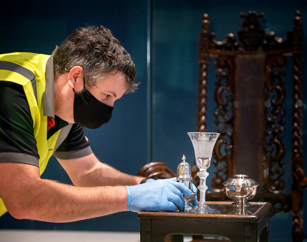 man in high vis jacket and mask lays out tableware in museum display
