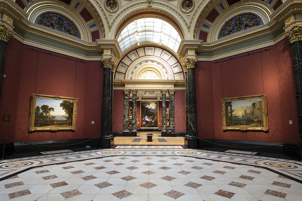 The photograph shows the inside of Gallery 36. The floor has white and red tiles. The walls are red and the photograph looks through to the next two galleries. There is a painting to the left and right with gold frames. 