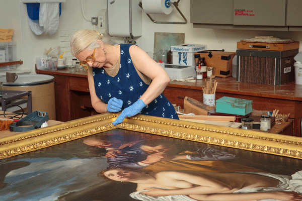 conservator works on large oil painting