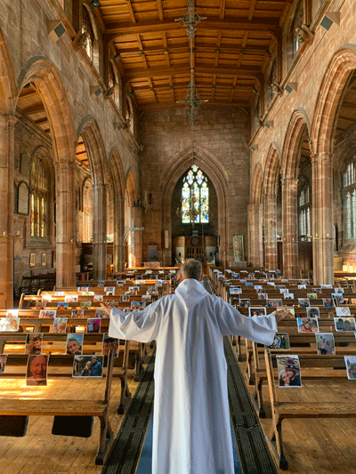 priest stands in empty church with pews full of the pictures of absent parishioners