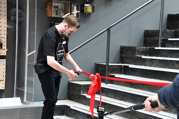 man in rainbow face mask opens the museum cutting ribbon with scissors