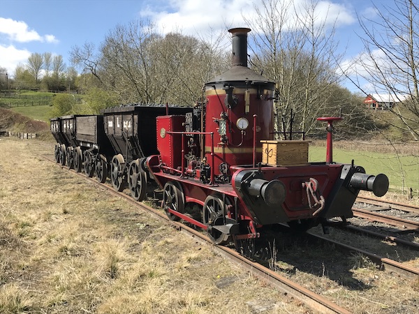 red steam locomotive with two trucks outside on tracks