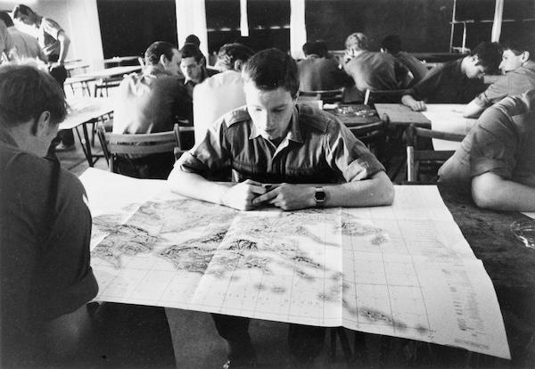 young man with digital watch looking at map in room surrounded by other soldiers