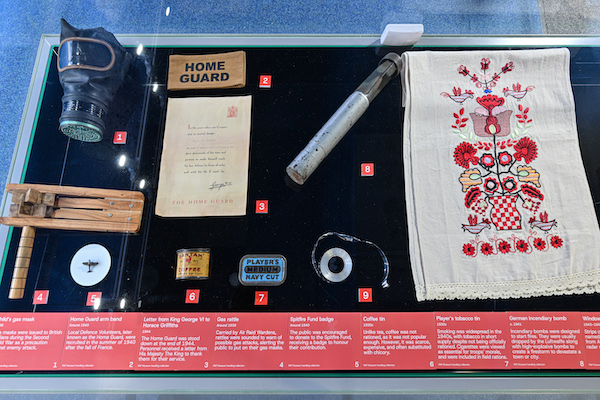 Photograph of a display case showing objects that relate to war and conflict including a gas mask and home guard arm band.