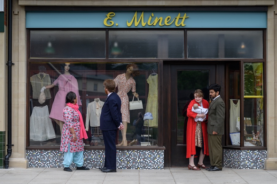 The shop front of E. Minetti Ladieswear, two people look into the shop window which displays women's clothes and two mannequins.