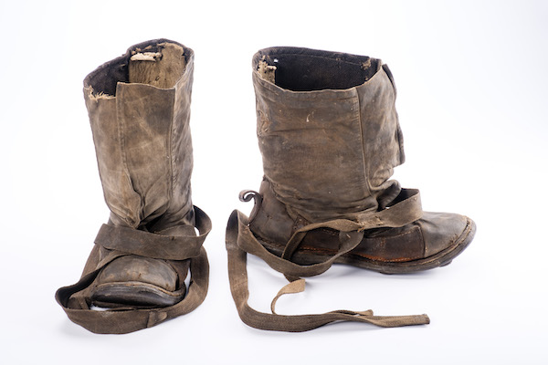 Photograph of a pair of well worn brown leather boots they are loose fitting and use leather straps to secure them. 