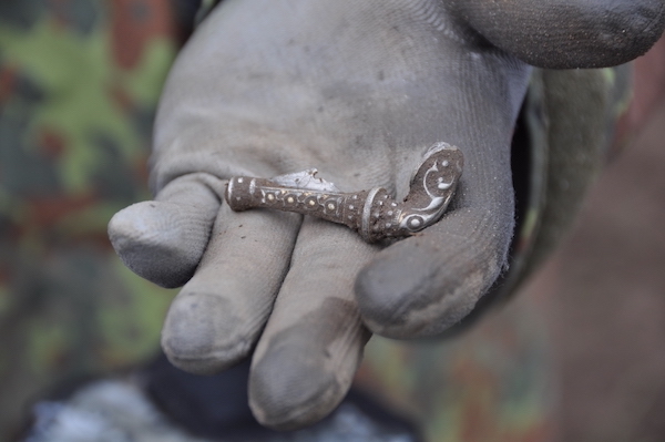 Photograph of a hand wearing a blue glove in the hand is a silver broach about the width of the hand in size it is silver and ornate.