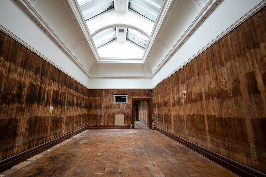 A gallery is stripped bare ready for renovation, their are bare wooden wall, the ceiling is white with light coming in through skylights