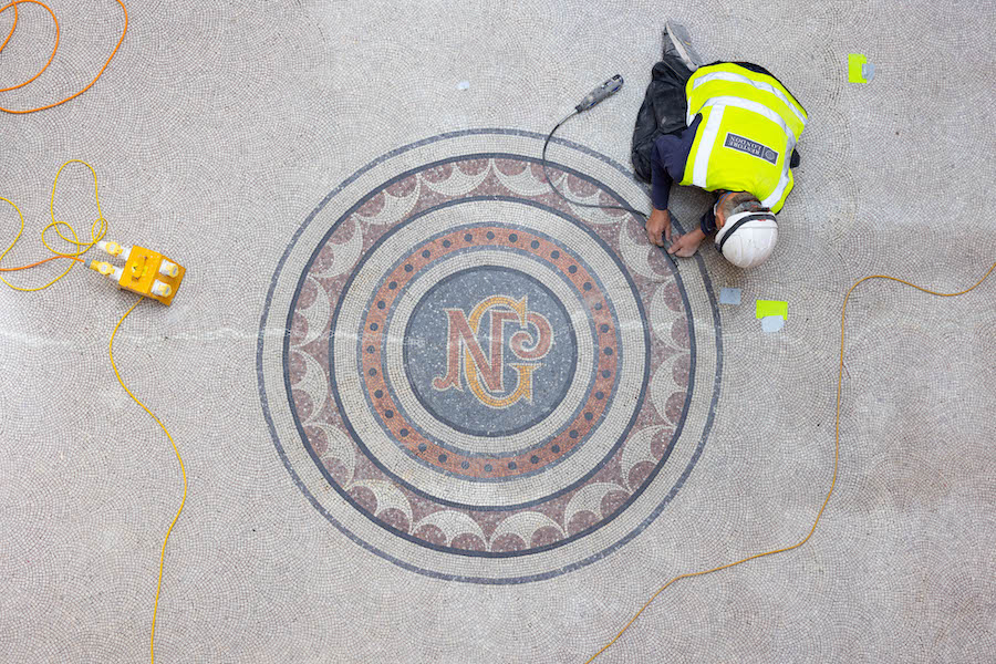 A workman kneels on a mosaic floor which has the NPG National Portrait Gallery initials displayed in a roundel