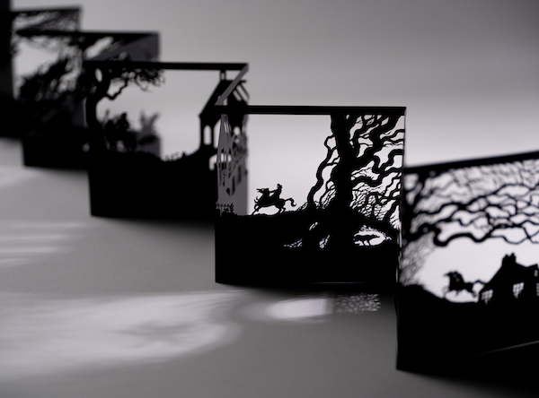 A silhouette of an art piece made of metal, it concertinas out showing a windswept tree and a man riding a horse across the landscape. 