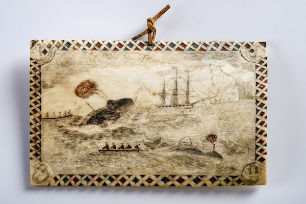 Photograph of an ivory plaque carved with a decorative border and a nautical scene showing ships and a whale. 