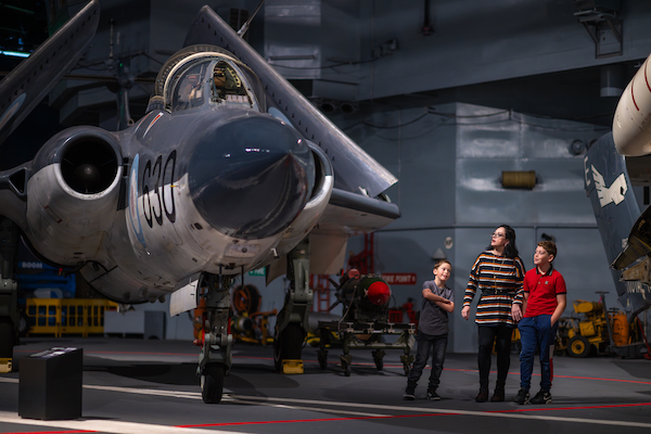 A family consisting of an adult and two children look up at an air craft in a museum hanger.