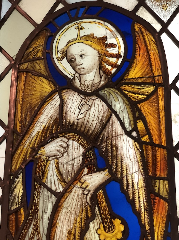 Stained glass window showing an angel, blue glass is in the background the angel is white and gold 