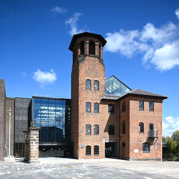 The exterior view of the Museum of Making at Derby Silk Mill. It is a glass and brick building with a tall tower.