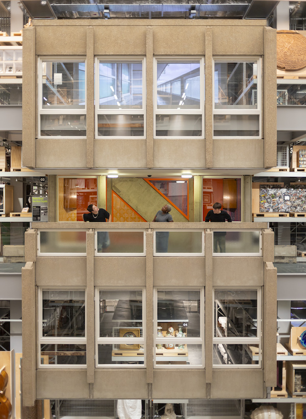 Photograph of the inside of a museum store, it shows an exterior section of a building (Robin Hood Gardens) with grey concrete sections and white framed windows.