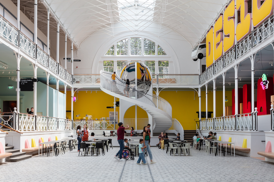 View of main atrium of Young V&A, the spaces has tables and chairs and a spiral staircase at the end